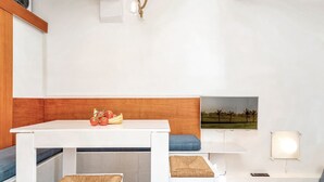 A white dining area with a wooden accent wall, a table with a fruit bowl, and a wall-mounted TV. - Neverland, Terre Marine (Portovenere)