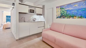 A modern kitchen with white cabinets, a pink sofa, and a colorful painting on the wall. - Via del Mare, Terre Marine (Riomaggiore)