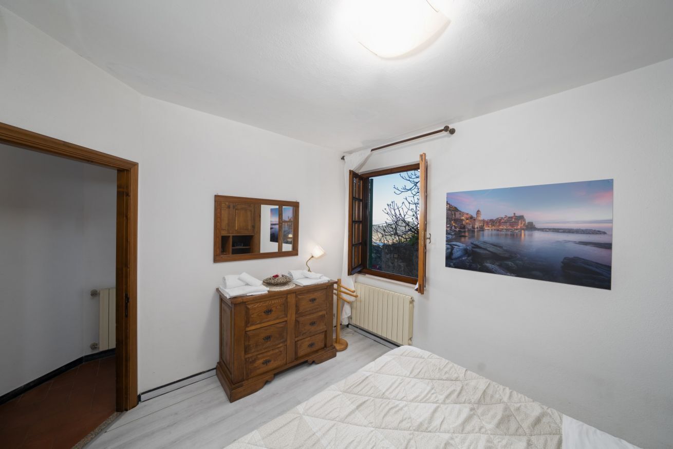 Un dormitorio con cama, cómoda de madera, espejo, ventana y un cuadro en la pared.