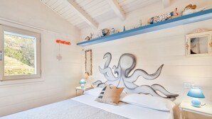 A bedroom with a large bed, a decorative headboard, a window with a view of greenery, and a shelf with various items. - The Chalet by the Sea, Terre Marine (Vernazza)