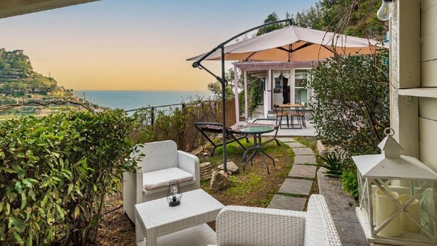 A patio with wicker furniture, a table, and a lantern. There is a view of the sea and a building in the background. - The Chalet by the Sea, Terre Marine (Vernazza)