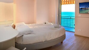 Een slaapkamer met een bed, nachtkastje, televisie en balkon met uitzicht op zee.