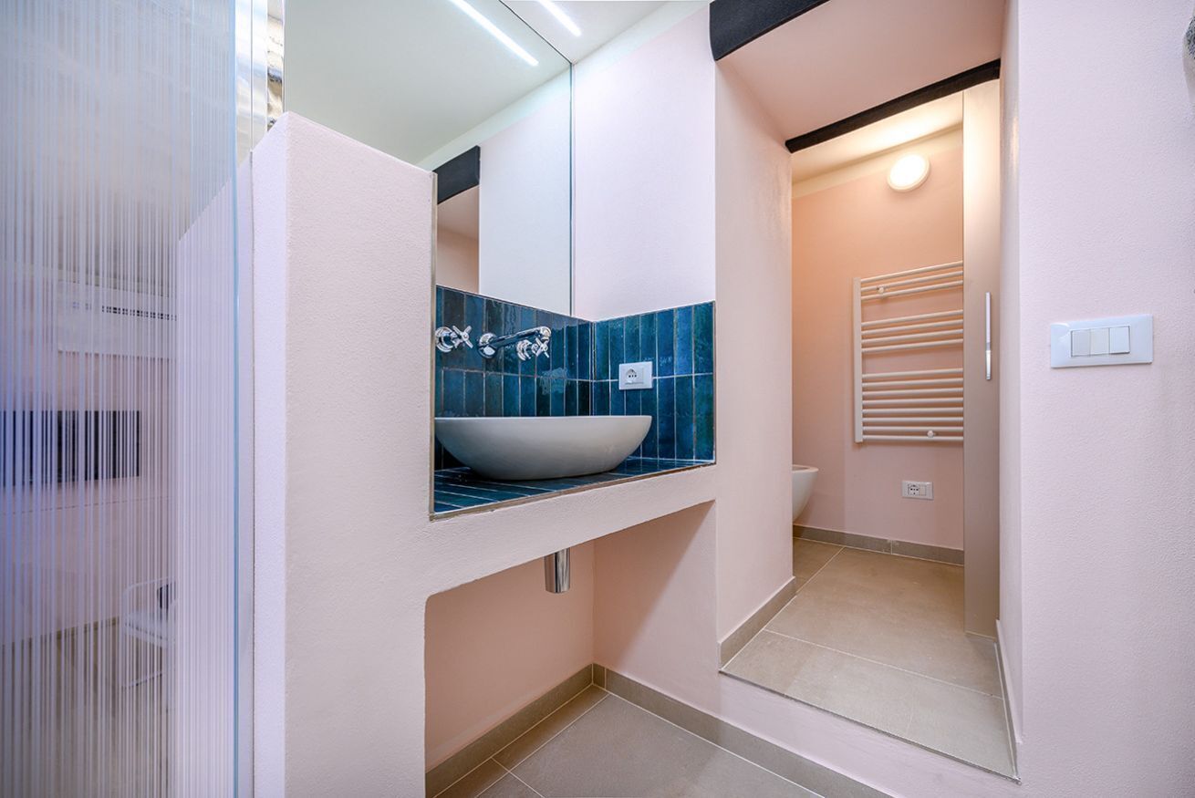 A bathroom with a white sink, blue-tiled backsplash, and a mirror above it.