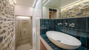 Een moderne badkamer met een stenen muur, een glazen douchecabine en een groot ovaal wastafel met een spiegel erboven.