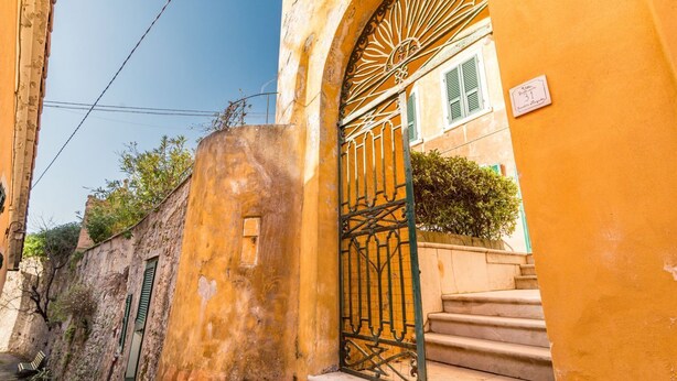 A narrow street with a yellow building featuring a wrought iron gate and steps leading to a door. - The Secret Garden, TerreMarine (Lerici)