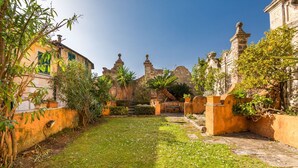 A courtyard with a grassy area, stone walls, and a building with a traditional architectural style. - The Secret Garden, TerreMarine (Lerici)