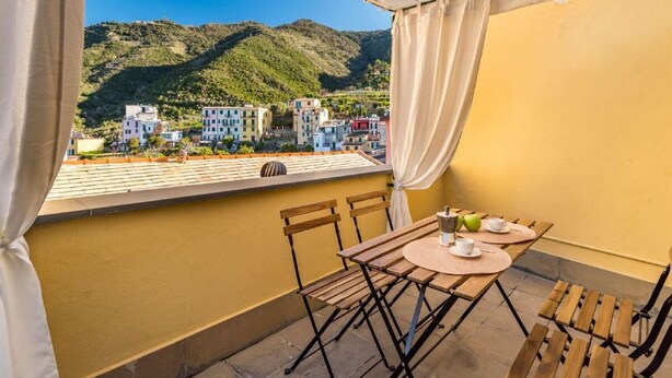 Un balcón con mesa y sillas, con vistas a edificios y colinas al fondo.