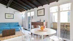 Un salón moderno con un sofá azul, una mesa de comedor redonda con fruteros, y vistas al exterior a través de amplios ventanales.