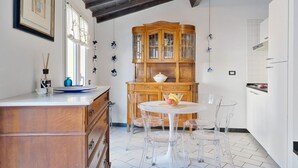 Una cocina con un armario de madera, una mesa redonda de comedor con sillas transparentes y un suelo de baldosas blancas.
