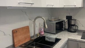 Een keuken met een spoelbak, een magnetron, een koffiezetapparaat en een snijplank.
