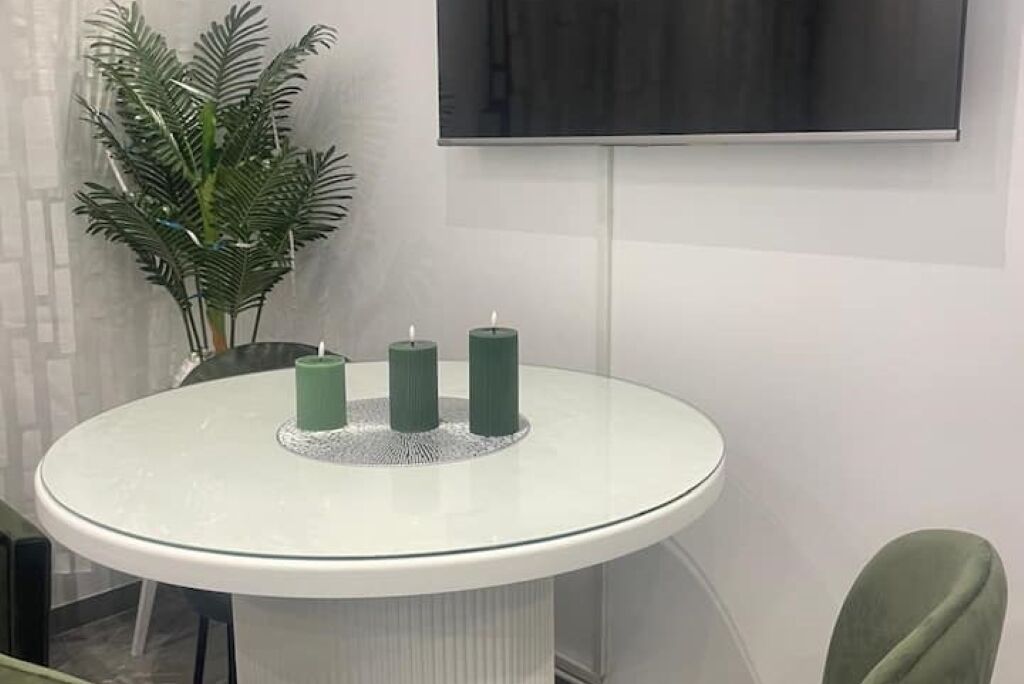 A round glass table with three green candles, a potted plant, and a flat-screen TV mounted on the wall.