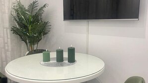 Een ronde glazen tafel met drie groene kaarsen, een potplant en een flatscreen televisie aan de muur.