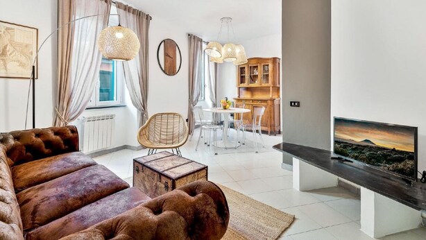 En moderne stue med en brun sofa, et spisebord med stole og et fjernsyn på et sort stativ.