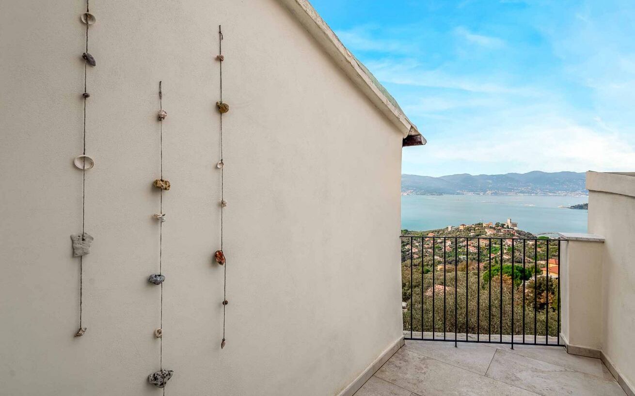 A balcony with a view of a coastal landscape, featuring a railing and a series of hanging items.