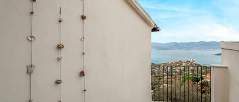A balcony with a view of a coastal landscape, featuring a railing and a series of hanging items.