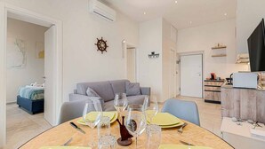 A modern living room with a dining area set for a meal, a grey sofa, and nautical-themed decor. - La Frida, Marine Lands (Lerici)