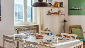 A dining area with a white table set for four, a black pendant light, and a view of the outdoors through a window.