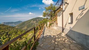 A stone staircase leading to a building with a balcony, surrounded by greenery and a mountainous landscape.