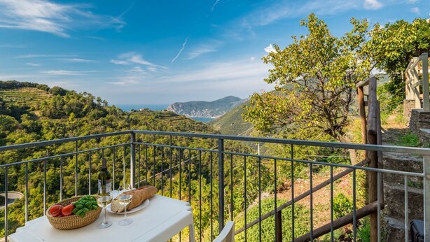 A balcony with a table set for a meal, overlooking a mountainous landscape.