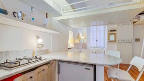A compact kitchen with a gas stove, a small refrigerator, and a dining area with a table and chairs.