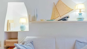 A living room with a white sofa, a small shelf with decorative items, and a sailboat model.