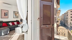 Un balcón con vistas a una calle de la ciudad, un sofá con cojines y una puerta con contraventanas.