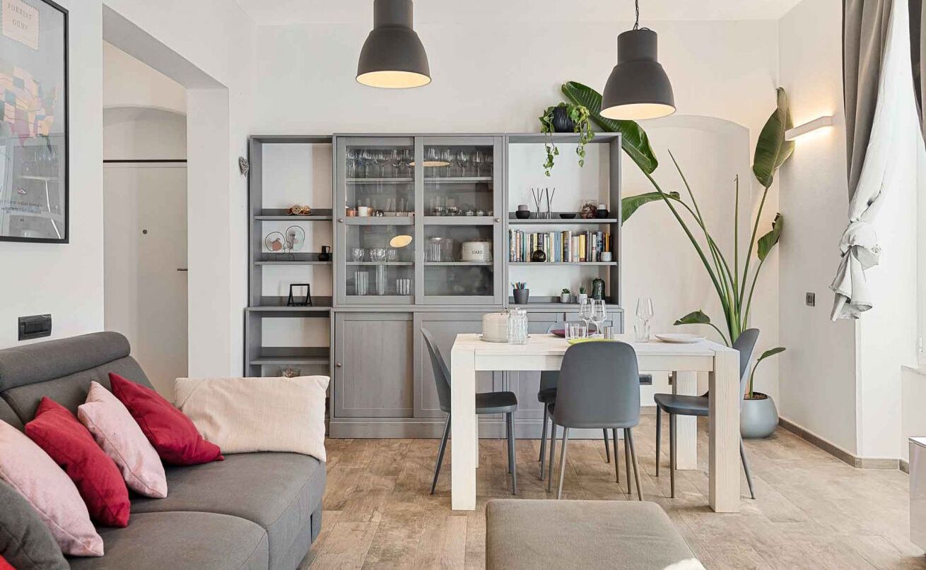 Un soggiorno moderno con un divano grigio, un tavolo da pranzo con sedie e un mobile contenitore grigio incassato con ante in vetro.