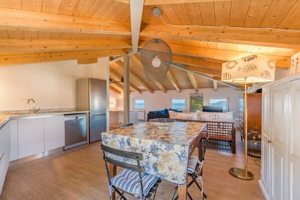 A spacious kitchen with wooden beams, a dining area with a patterned tablecloth, and a cozy seating area with cushions.