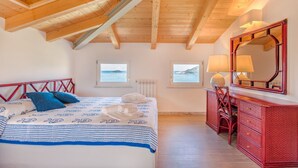 A bedroom with a wooden ceiling, a bed with blue and white bedding, a red dresser, and a large mirror. - Viewpoints, nature, walks and sea (Lerici)