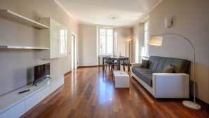 A modern living room with a flat-screen TV, a sofa, a coffee table, and a dining area with a table and chairs.