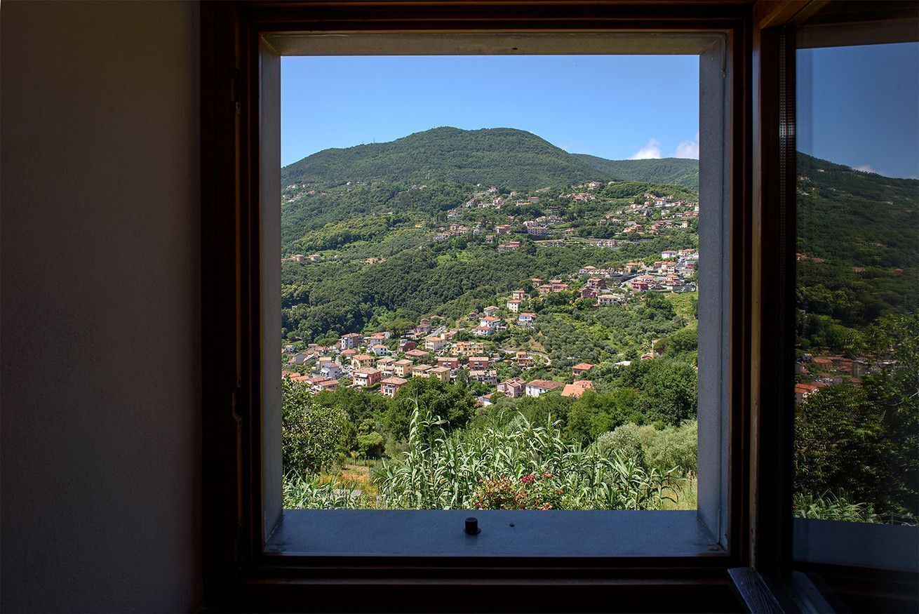 Vista desde una ventana de un pueblo en la ladera, con edificios y vegetación.