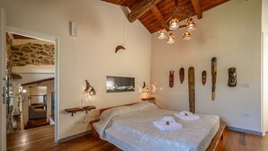Un dormitorio con cama de madera, pared de piedra y techo de madera. Hay luces fijadas a la pared y un cuadro enmarcado.