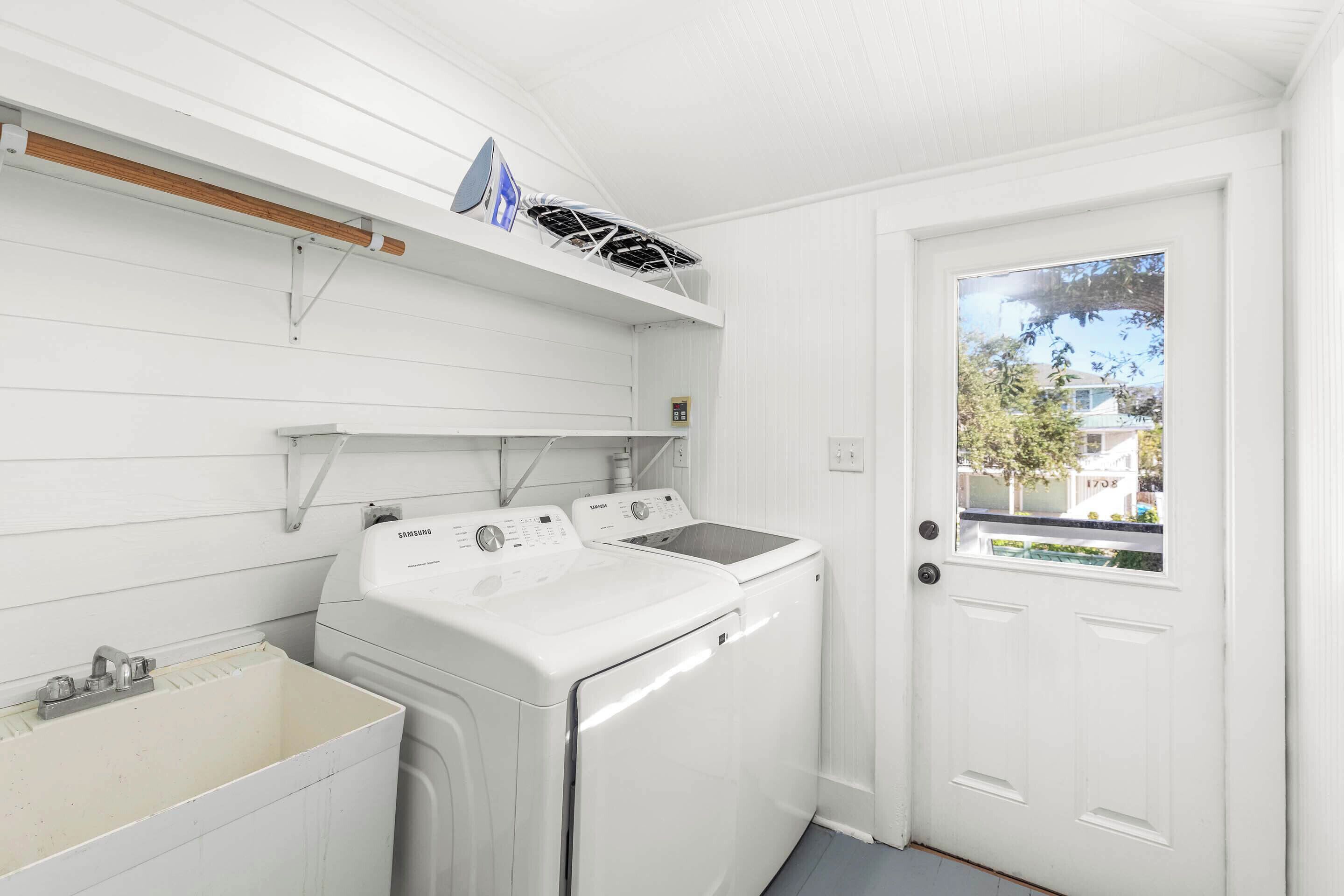 A laundry room with two white washers and a sink.