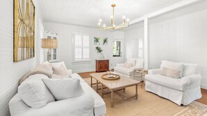 Un salon spacieux, meublé de blanc, avec une table basse en bois et un lustre.