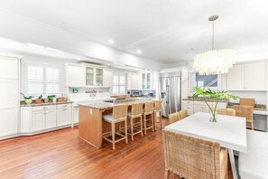 A modern kitchen with white cabinetry, a central island with bar stools, and a dining area with wicker furniture.