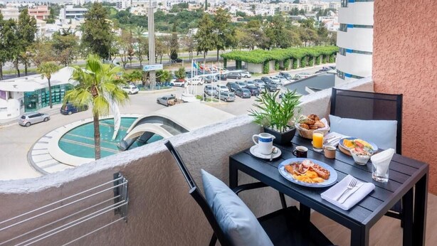 Un balcon avec une table préparée pour le petit-déjeuner, donnant sur un parking et une piscine.
