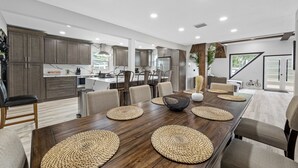 A spacious kitchen with modern appliances, a dining area with a long wooden table, and a view of the outdoors. - Luxury A-Frame Escape: 6BR, 4BA, Pool, Pickleball, Cinema & Ultimate Relaxation! (Thonotosassa)