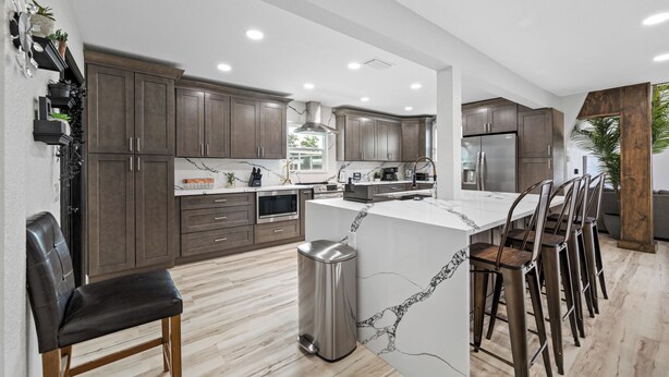 A modern kitchen with dark wood cabinets, a marble island, stainless steel appliances, and a dining area with bar stools. - Luxury A-Frame Escape: 6BR, 4BA, Pool, Pickleball, Cinema & Ultimate Relaxation! (Thonotosassa)