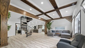A spacious living area with a modern staircase, a gray sofa, and a dining area. - Luxury A-Frame Escape: 6BR, 4BA, Pool, Pickleball, Cinema & Ultimate Relaxation! (Thonotosassa)