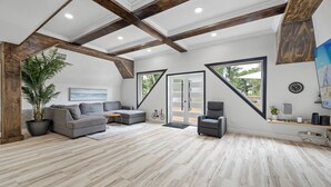 A spacious living room with a grey sectional sofa, a small grey armchair, and a potted plant. There are large windows with a view of the outdoors. - Luxury A-Frame Escape: 6BR, 4BA, Pool, Pickleball, Cinema & Ultimate Relaxation! (Thonotosassa)