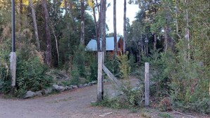 Ein bewaldetes Gebiet mit einem Feldweg, der zu einer Hütte mit einem Metalldach führt.