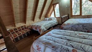 Ein gemütliches Schlafzimmer im Dachgeschoss mit zwei Betten, Holzbalken und großen Fenstern.