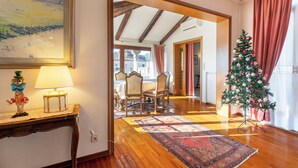 Une pièce avec un plancher en bois, une table à manger avec des chaises, un sapin de Noël et un tableau accroché au mur.