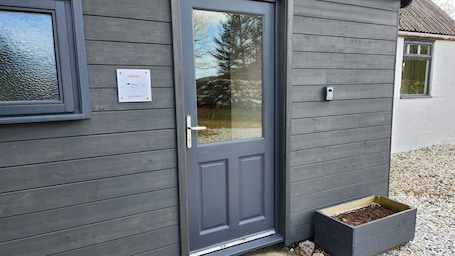 A grey wooden door with a glass panel, a mailbox, and a planter box with soil.