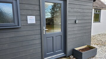 Una puerta de madera gris con un panel de vidrio, un buzón y una jardinera con tierra.