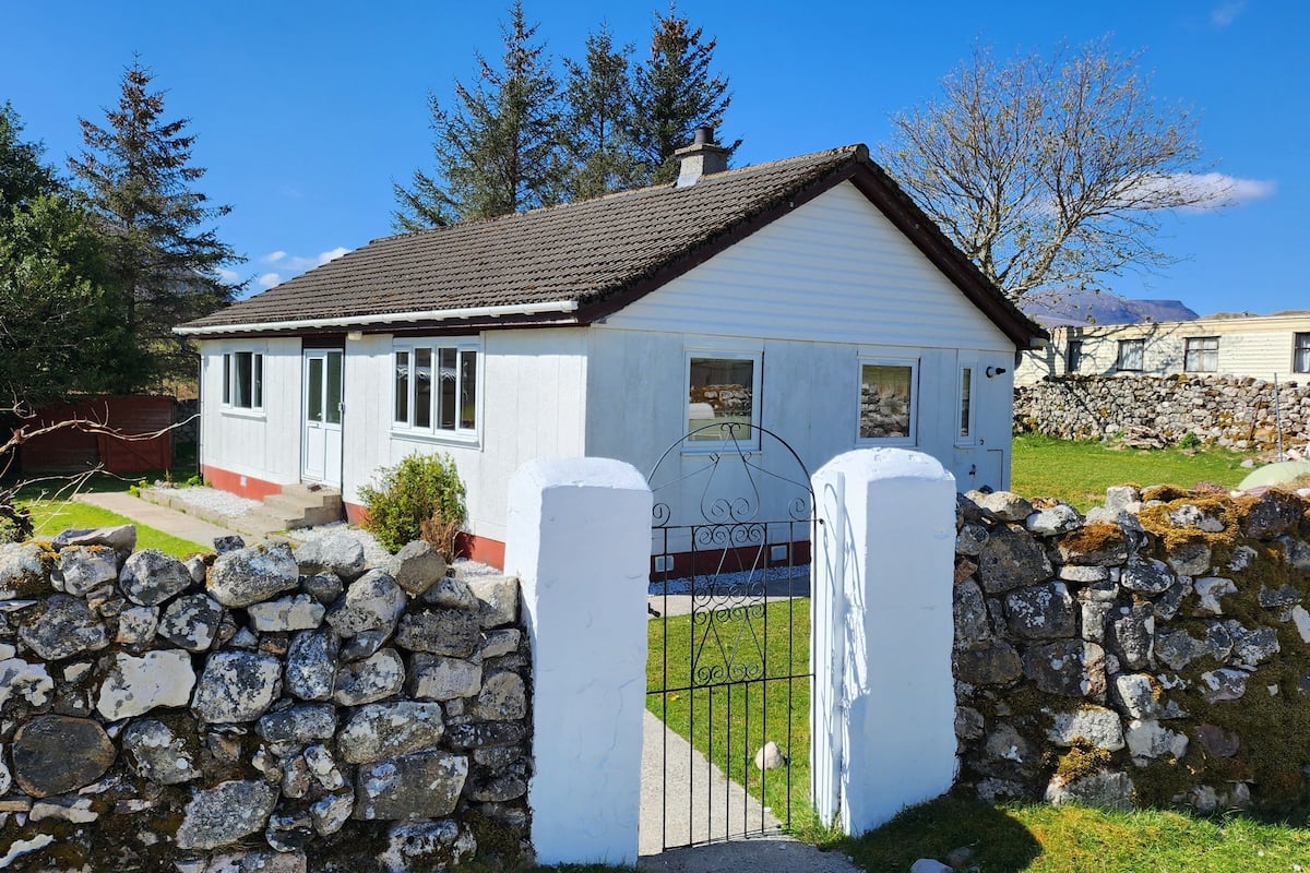 A white house with a stone wall and a metal gate.