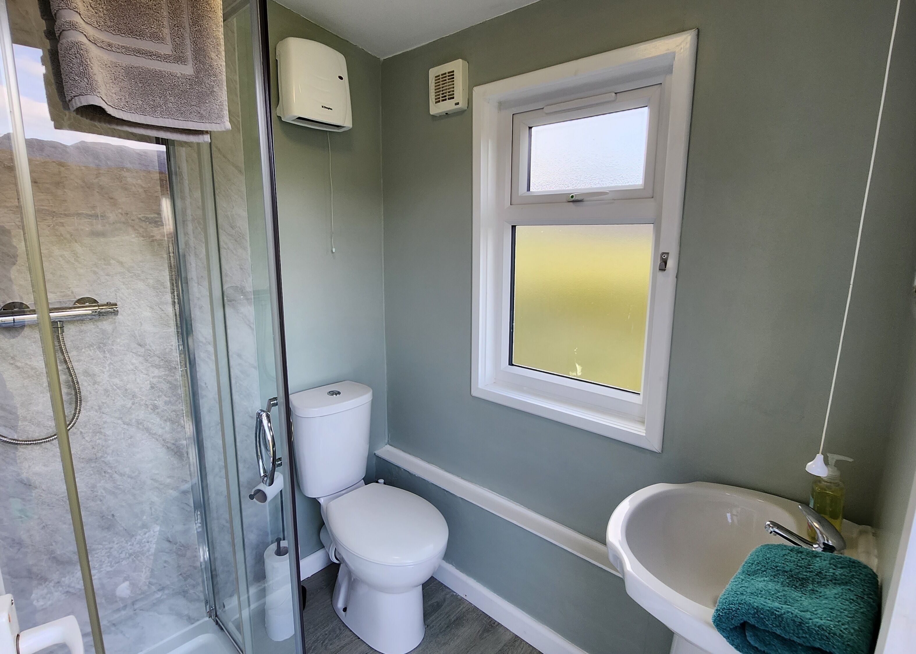 A bathroom with a glass shower enclosure, a toilet, a window, and a sink.