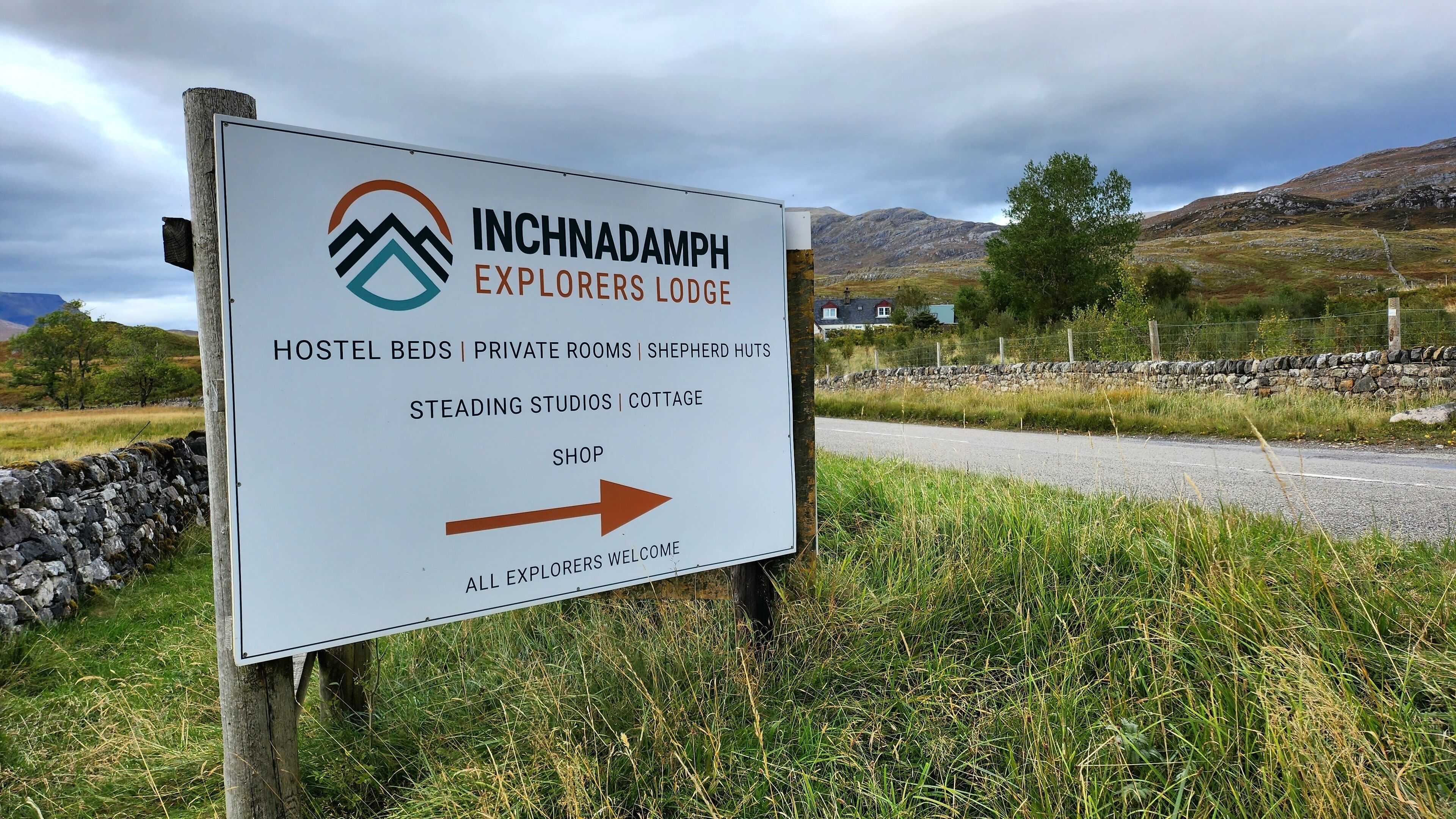 Señal de Inchnadamph Explorers Lodge que enumera servicios como camas de albergue, habitaciones privadas, cabañas de pastor y una tienda.