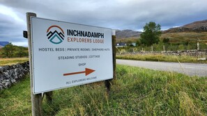 A sign for Inchnadamph Explorers Lodge listing amenities like hostel beds, private rooms, shepherd huts, and a shop.