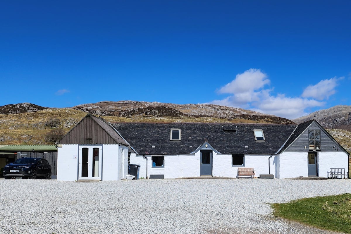 A white building with a gravel driveway, a car, and a picnic table.